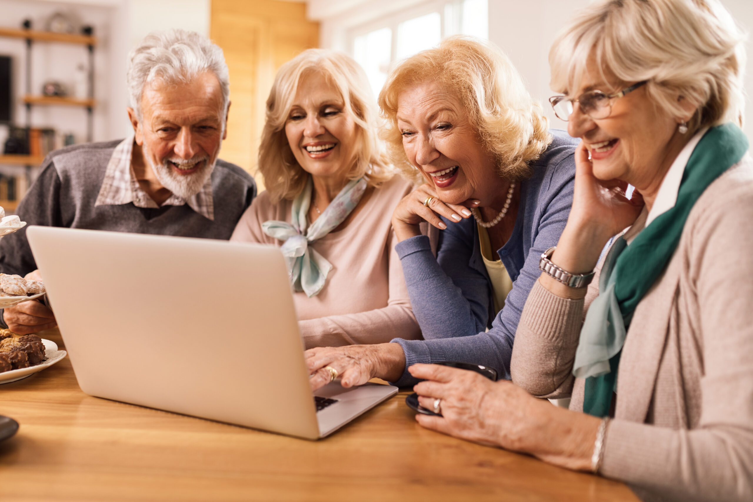 Grupa seniorów spędzających czas razem i korzystających z internetu na komputerze w domu.