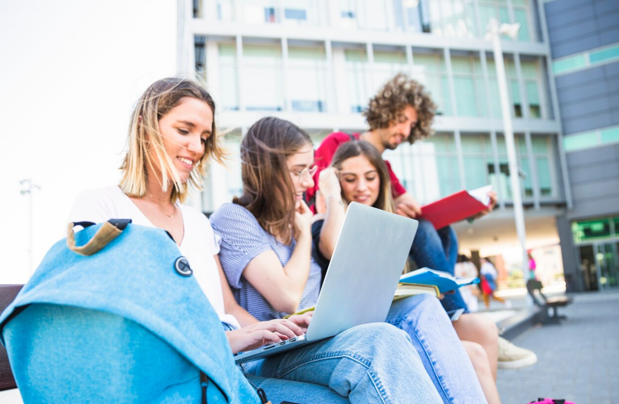Grupa studentów uczących się wspólnie przed budynkiem uczelni.